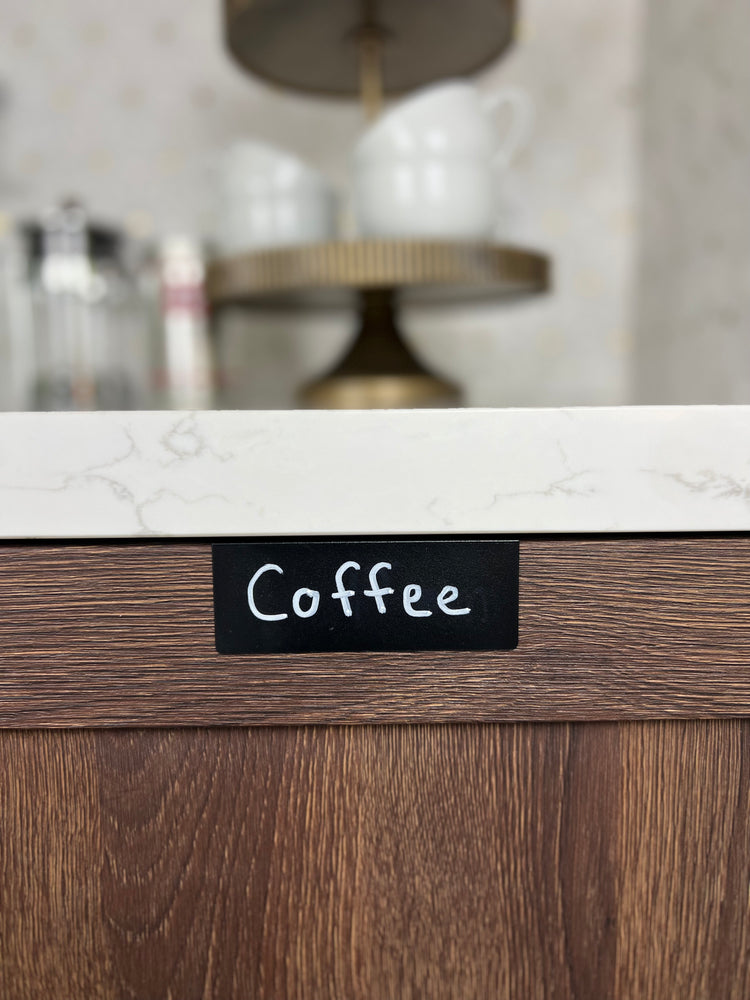 Black TidyPop labels reading serveware, pots, and pans on maple kitchen cabinets