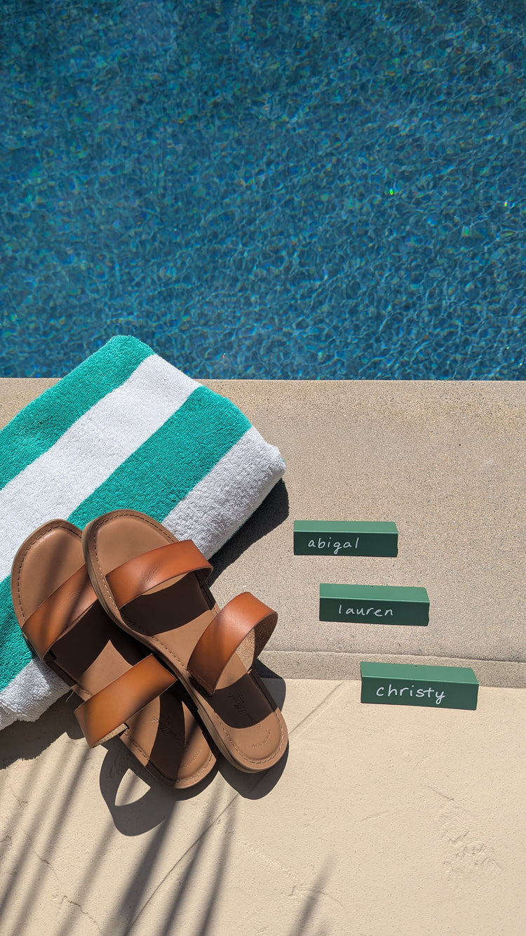 Sage TidyPop place cards with names by a pool next to sandals and a towel