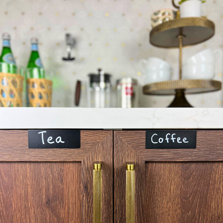 Black TidyPop labels that say Tea and Coffee on wood cabinets at a coffee bar